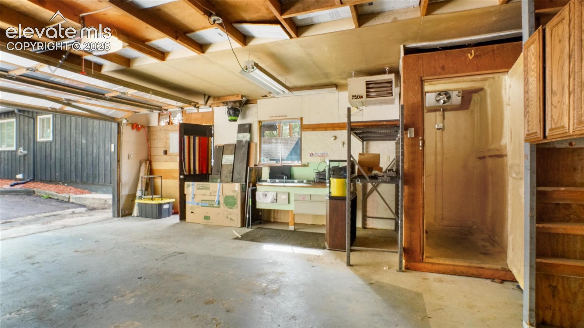 Concrete floor, exposed wood beam ceiling, fluorescent lighting, attached cabinetry, built-in cold storage unit and heater.