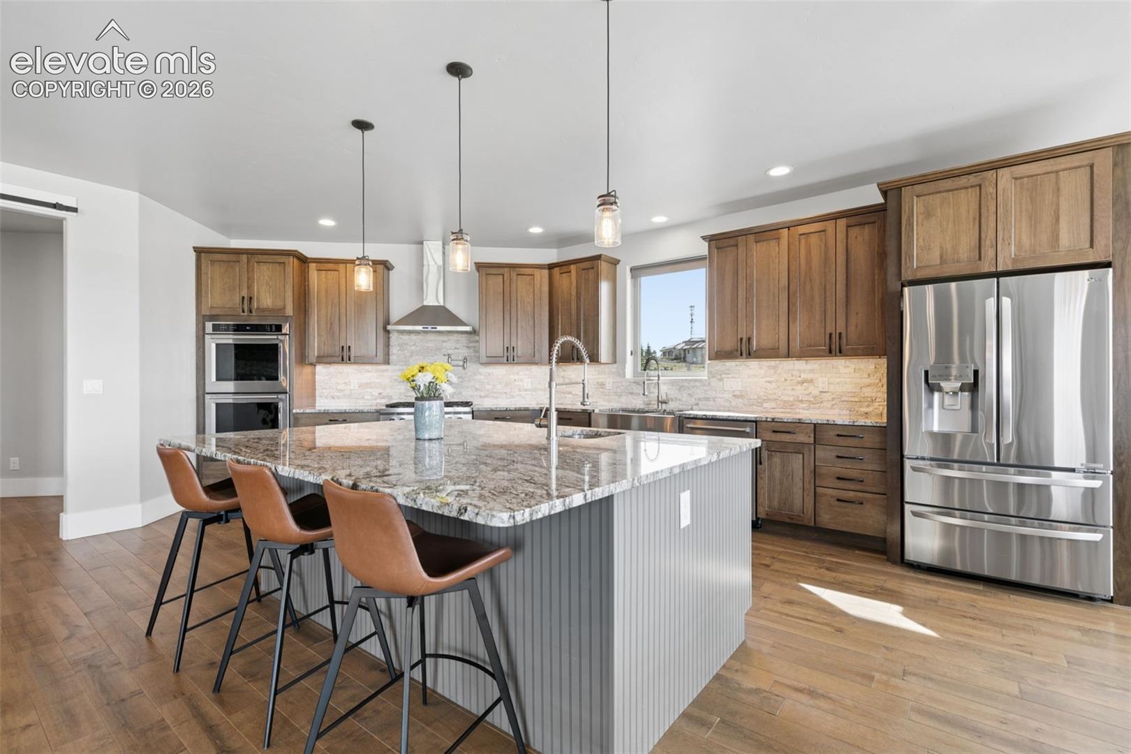 Gourmet kitchen featuring wood-finish cabinetry, stainless steel appliances, a large center island with a stone countertop, pendant lighting, and wood-finish flooring