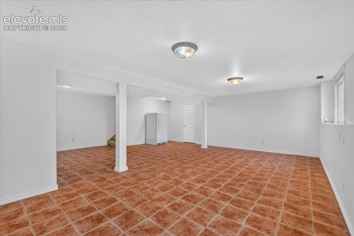 Open-concept interior featuring ceramic tile flooring, neutral walls, structural support columns, dual flush-mount ceiling lighting, and an integrated appliance