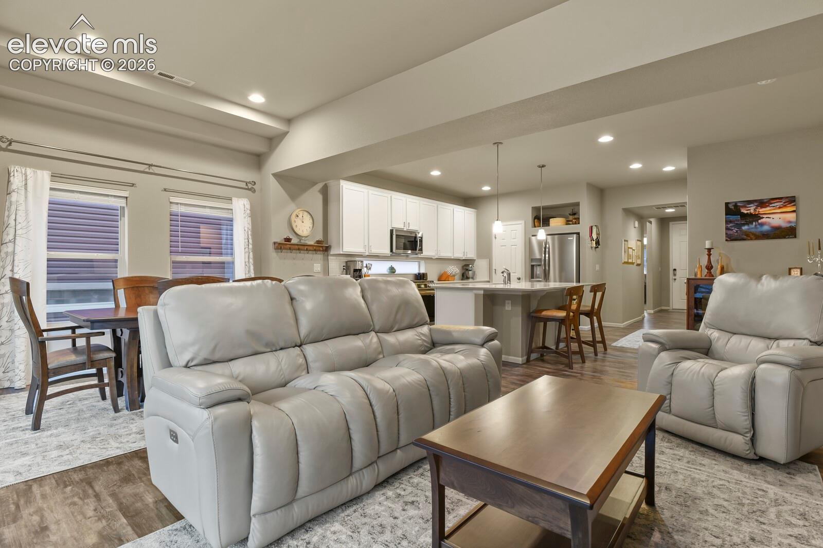 Open-concept interior featuring wood-finish luxury tile flooring, recessed lighting, white cabinetry, a center island with pendant lighting, and a tray ceiling