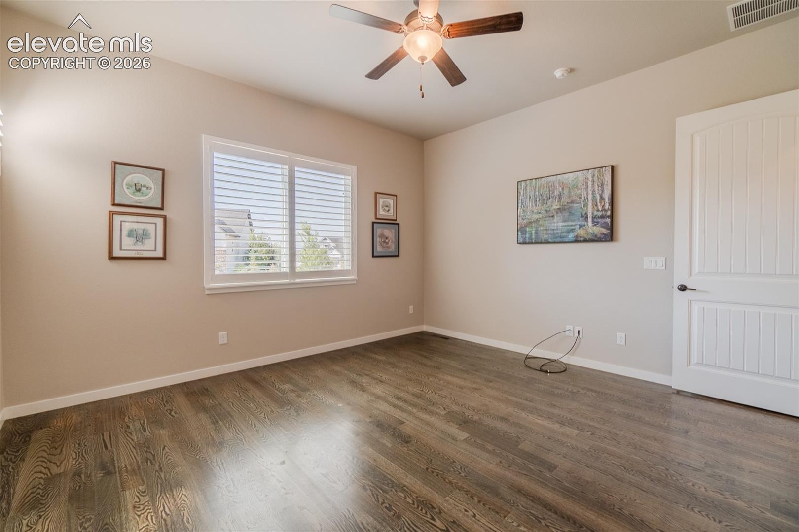 Spacious room featuring wood-finish flooring, a ceiling fan with integrated lighting, and a window with white blinds