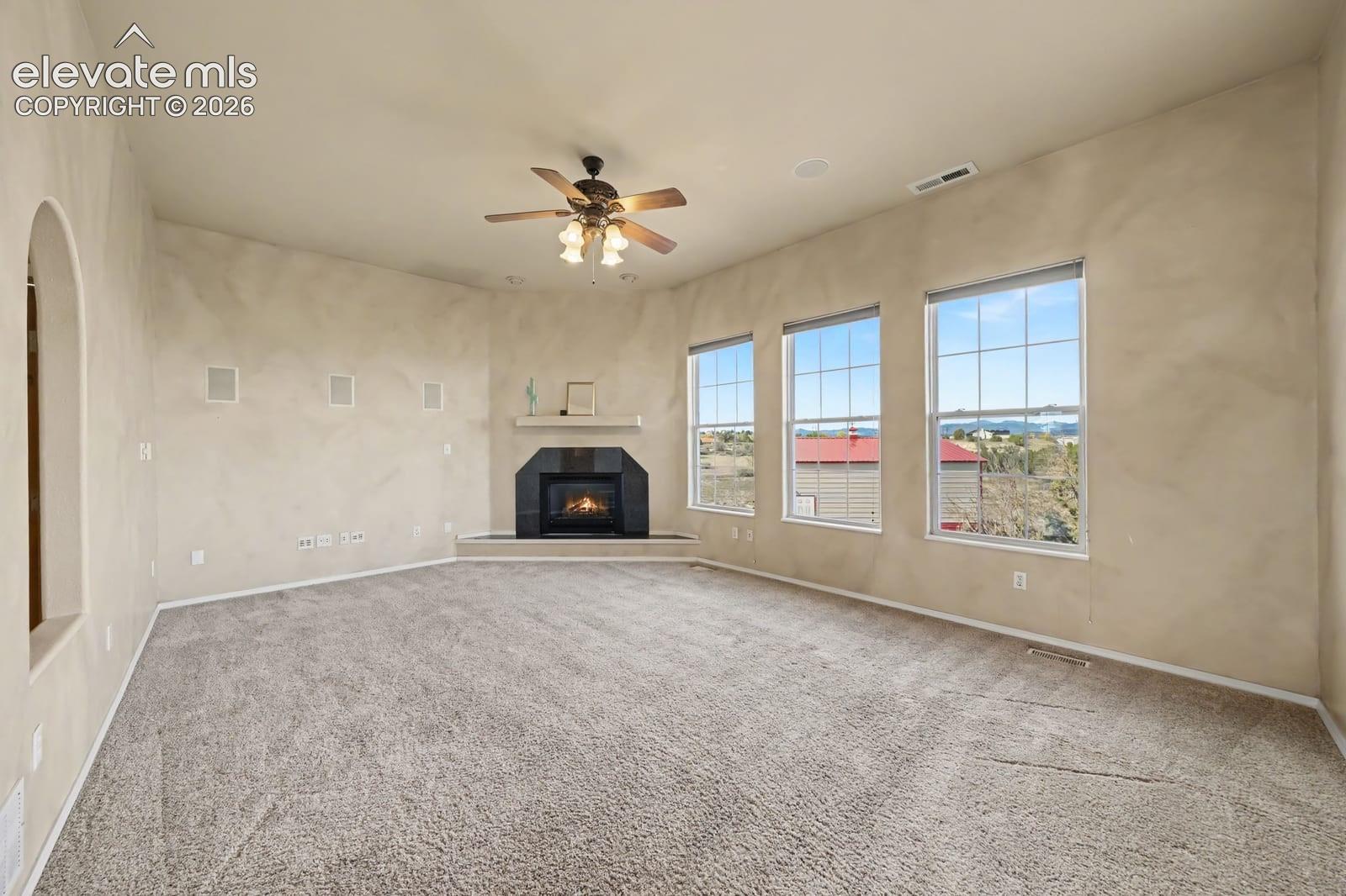Neutral-toned room featuring a corner fireplace with a dark surround and mantel, triple pane windows, arched entryway, and ceiling fan with integrated lighting