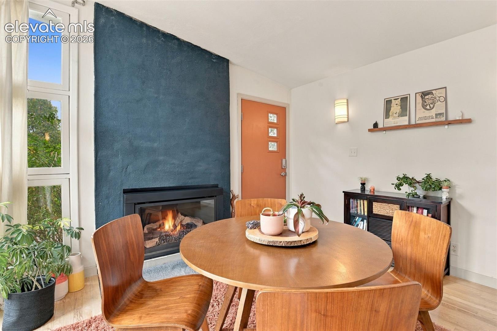 Living area featuring a floor-to-ceiling textured fireplace surround, wood-finish flooring, tall vertical window panels, wall-mounted lighting, and a solid-core door with glass inserts