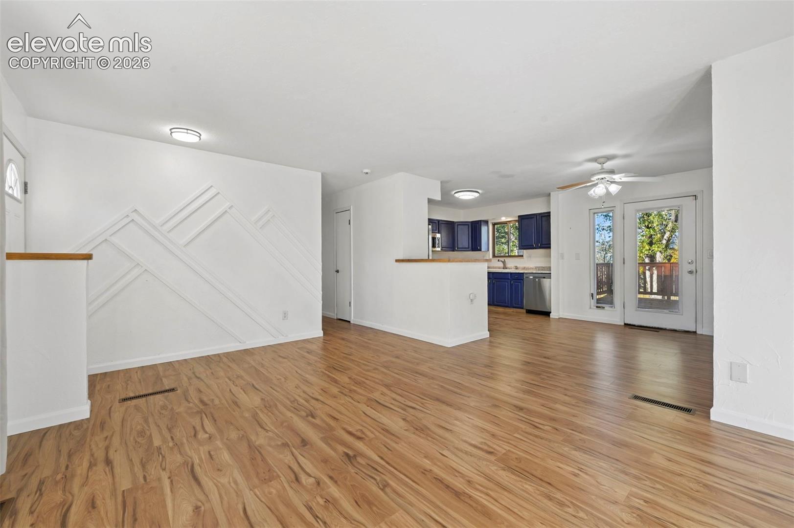 Living space featuring LVP flooring, mountainous geometric accent wall, flush-mount lighting, and a partial wall divider with a wooden cap