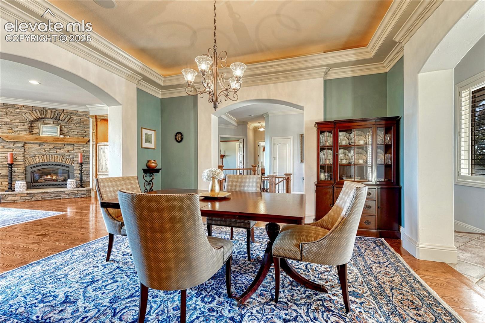 Formal dining area featuring tray ceilings with crown molding, a multi-arm chandelier, wood-finish flooring, and arched architectural openings