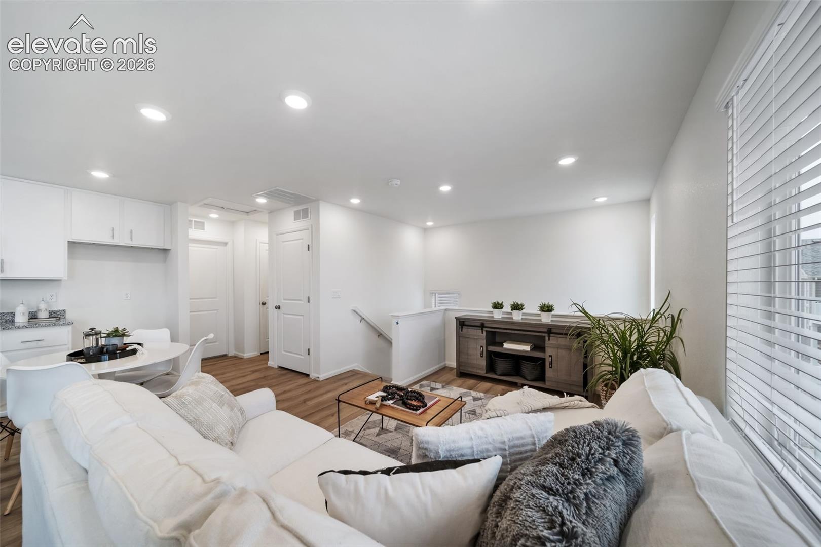 Recessed lighting, wood-finish flooring, white cabinetry, white walls, and a staircase with a white railing