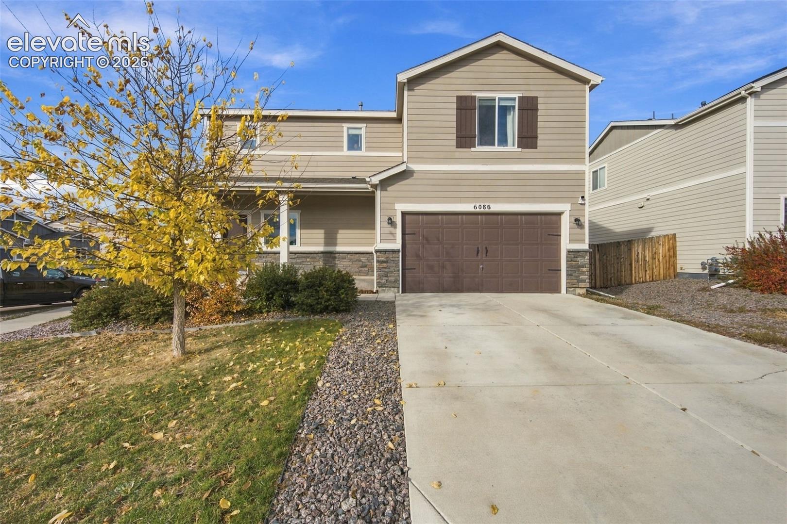 Two-story exterior featuring horizontal siding, stone veneer accents, decorative window shutters, and an attached two-car garage with a concrete driveway
