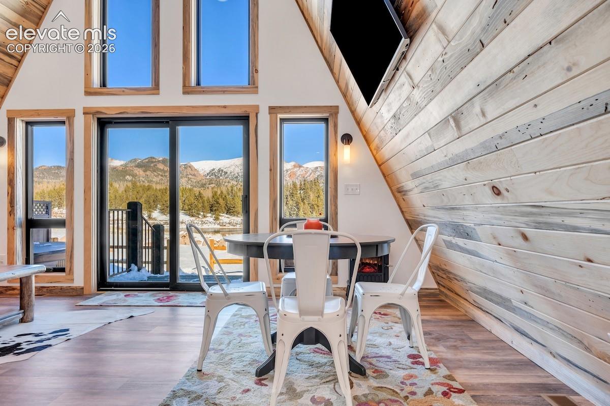 A-frame interior featuring vaulted ceilings with exposed wood-plank walls, floor-to-ceiling windows, sliding glass door access to a deck, and wood-finish flooring