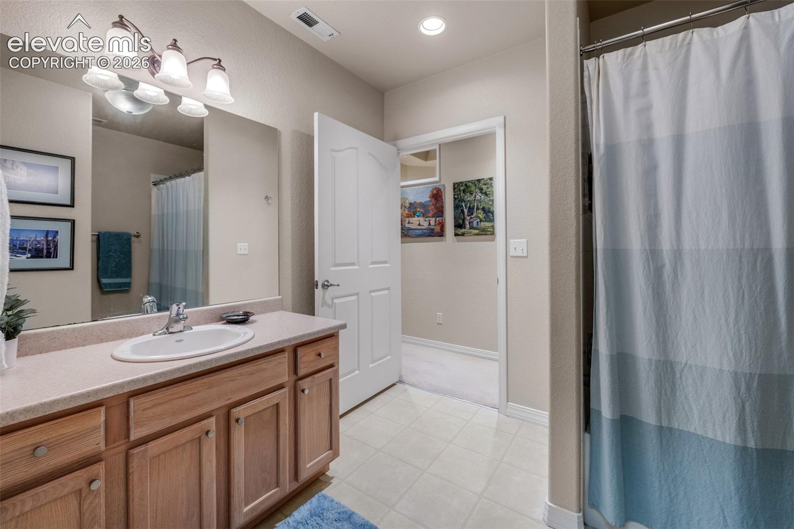Bathroom featuring a vanity with wood-finish cabinetry, a single basin sink, a light-toned countertop, and a wall-mounted light fixture