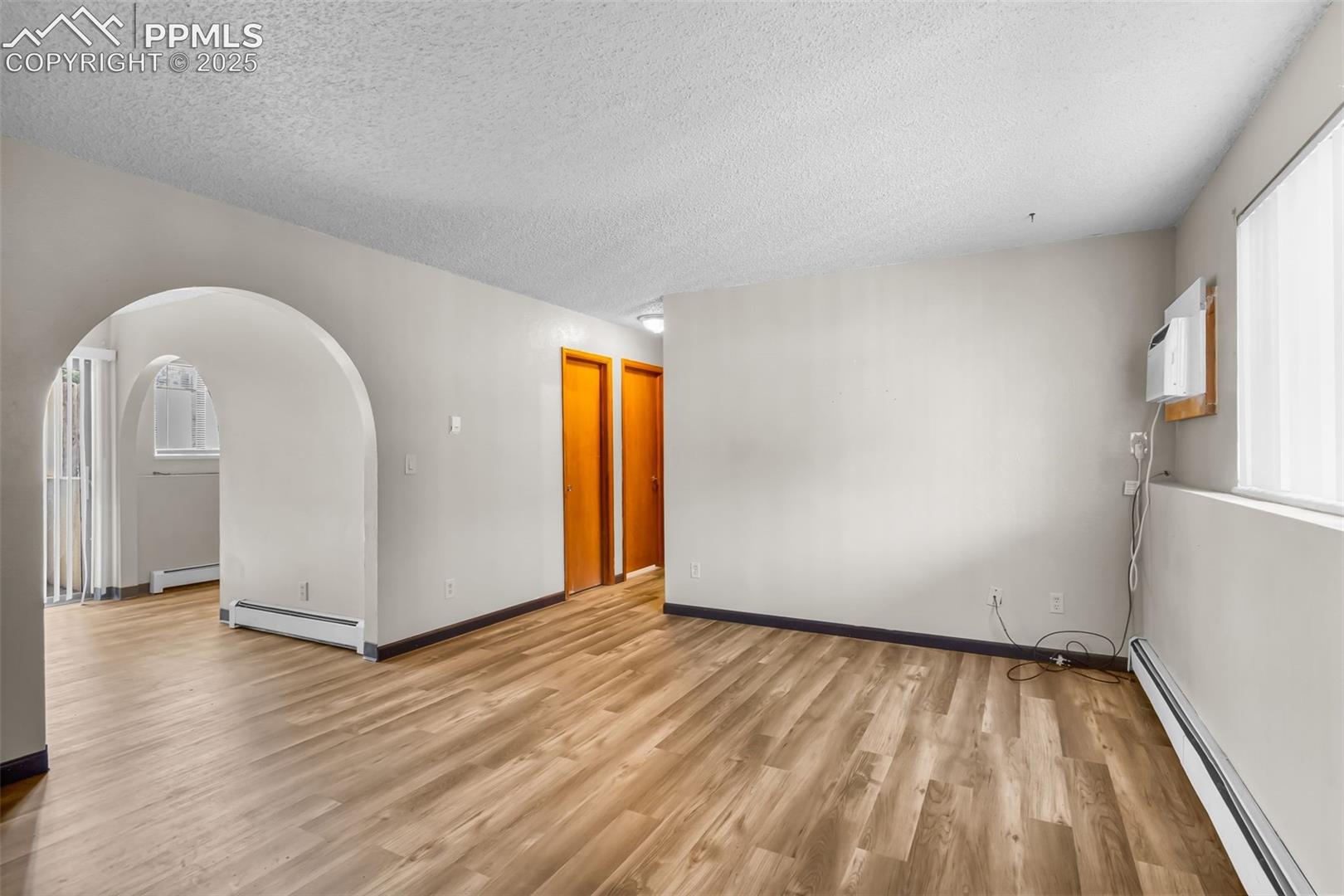 Spare room featuring healthy amount of natural light, a baseboard heating unit, arched walkways, light wood finished floors, and a textured ceiling