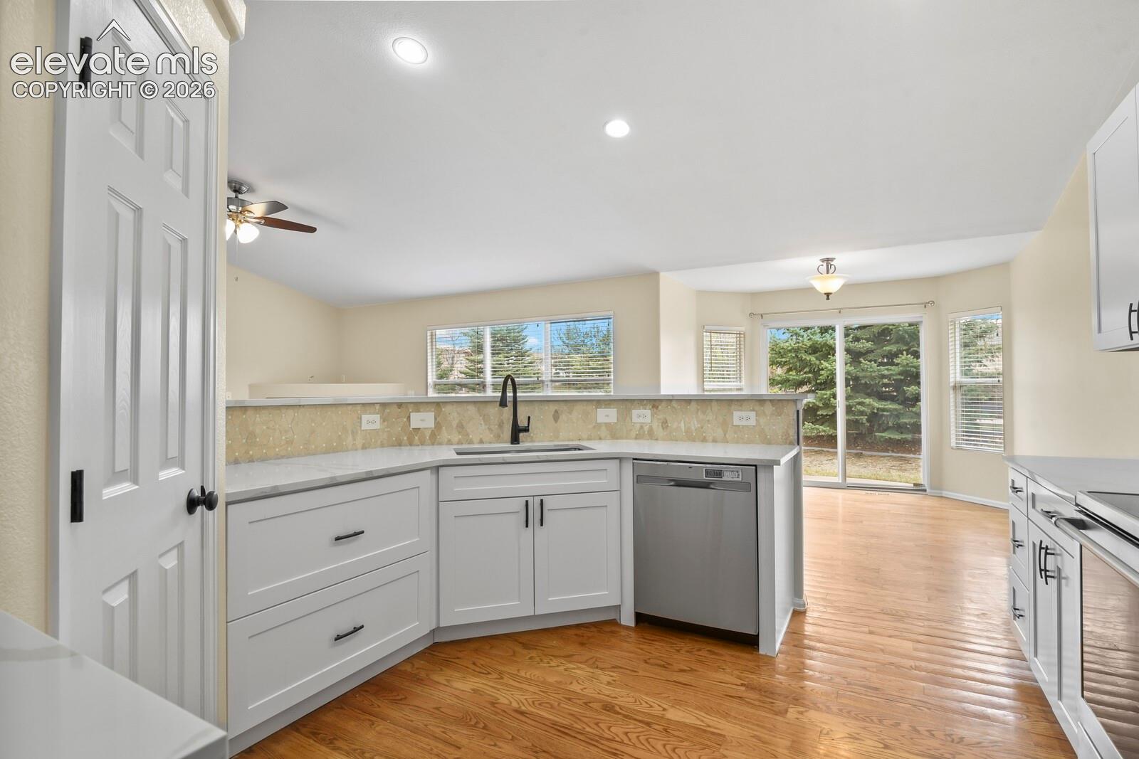 Contemporary kitchen featuring white cabinetry, light-colored countertops, a stainless steel dishwasher, and a bronze faucet