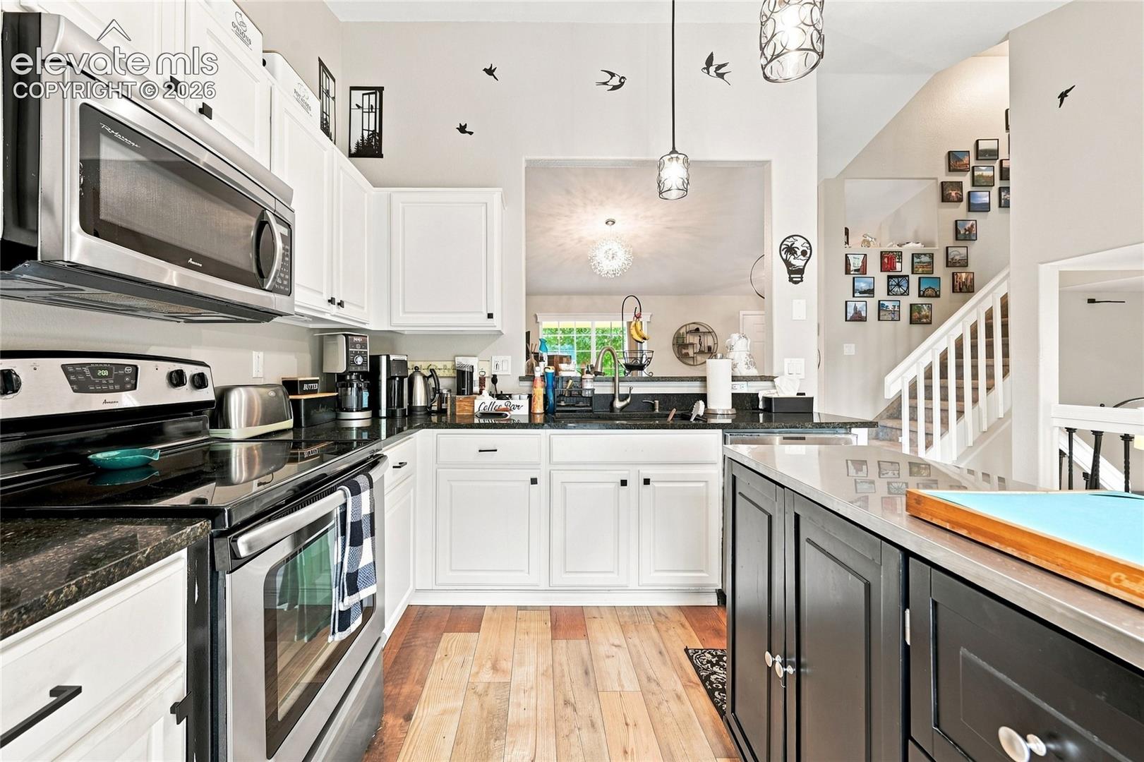 Kitchen featuring white shaker-style cabinetry, dark stone countertops, stainless steel appliances, a contrasting dark central island, and wood-finish flooring