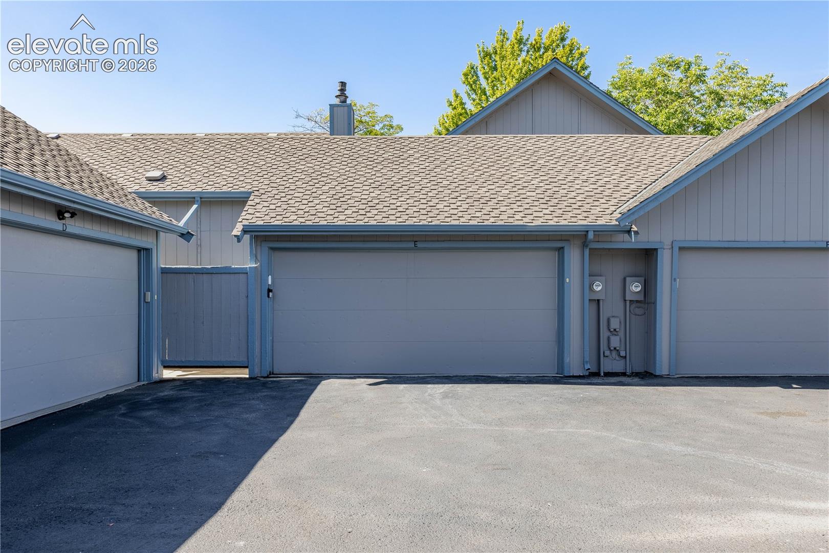 Exterior view featuring dual-car garage bays, vertical panel siding, asphalt shingle roofing, and a privacy fence