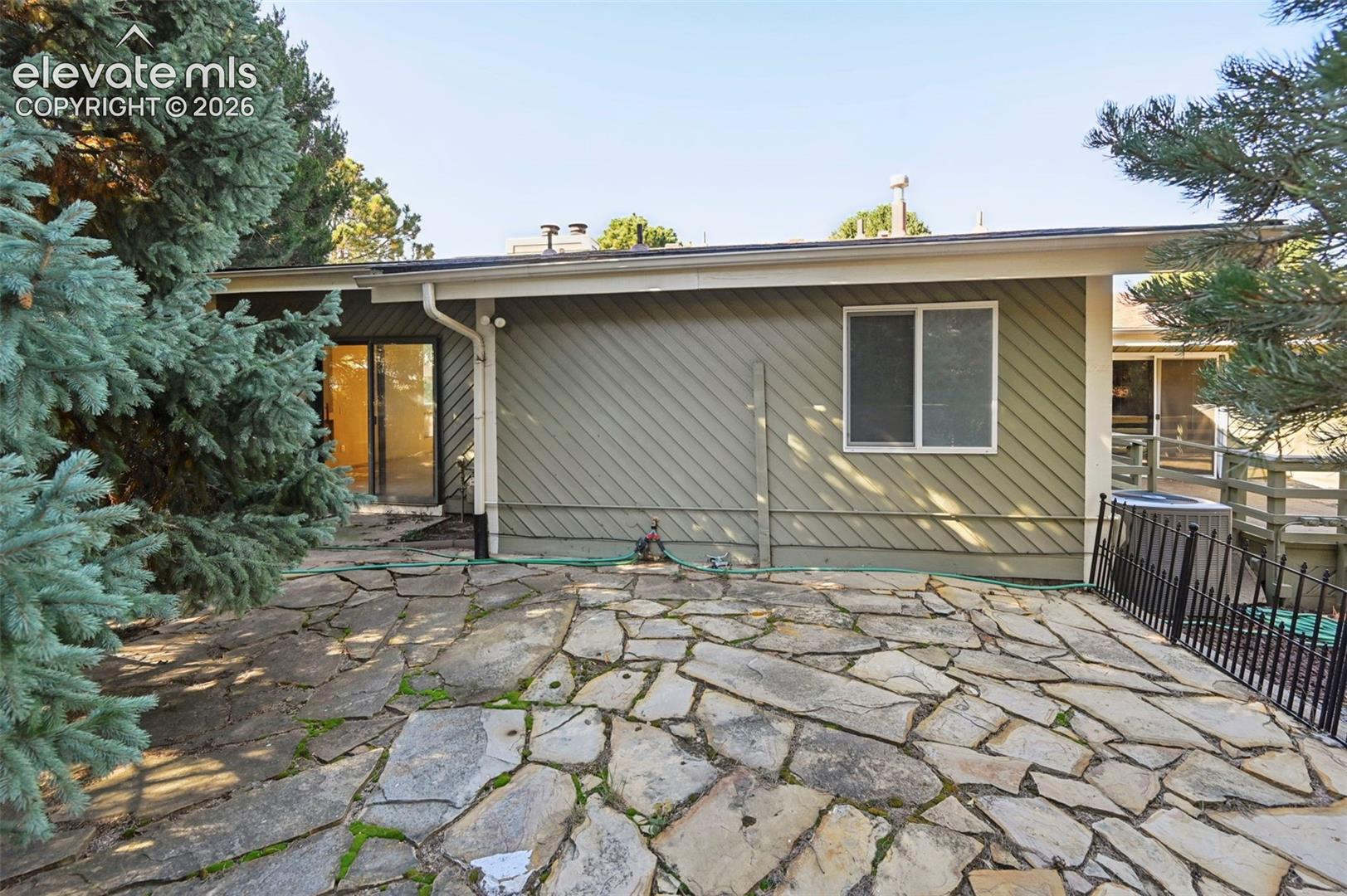 Exterior featuring diagonal wood-style siding, flagstone patio, sliding glass door, and metal perimeter fencing