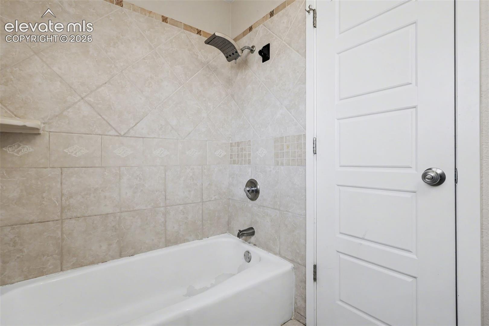 Bathtub with a showerhead featuring neutral-toned diagonal wall tile, decorative tile accents, and a white four-panel door