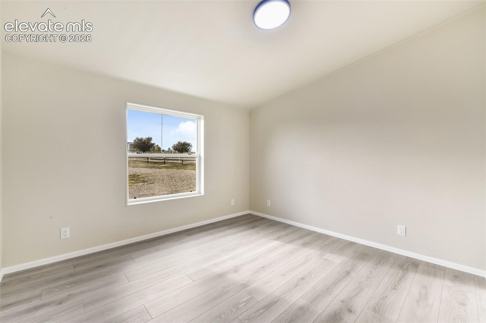Light wood-finish flooring, neutral wall paint, white trim, single window, and a flush-mount ceiling light fixture