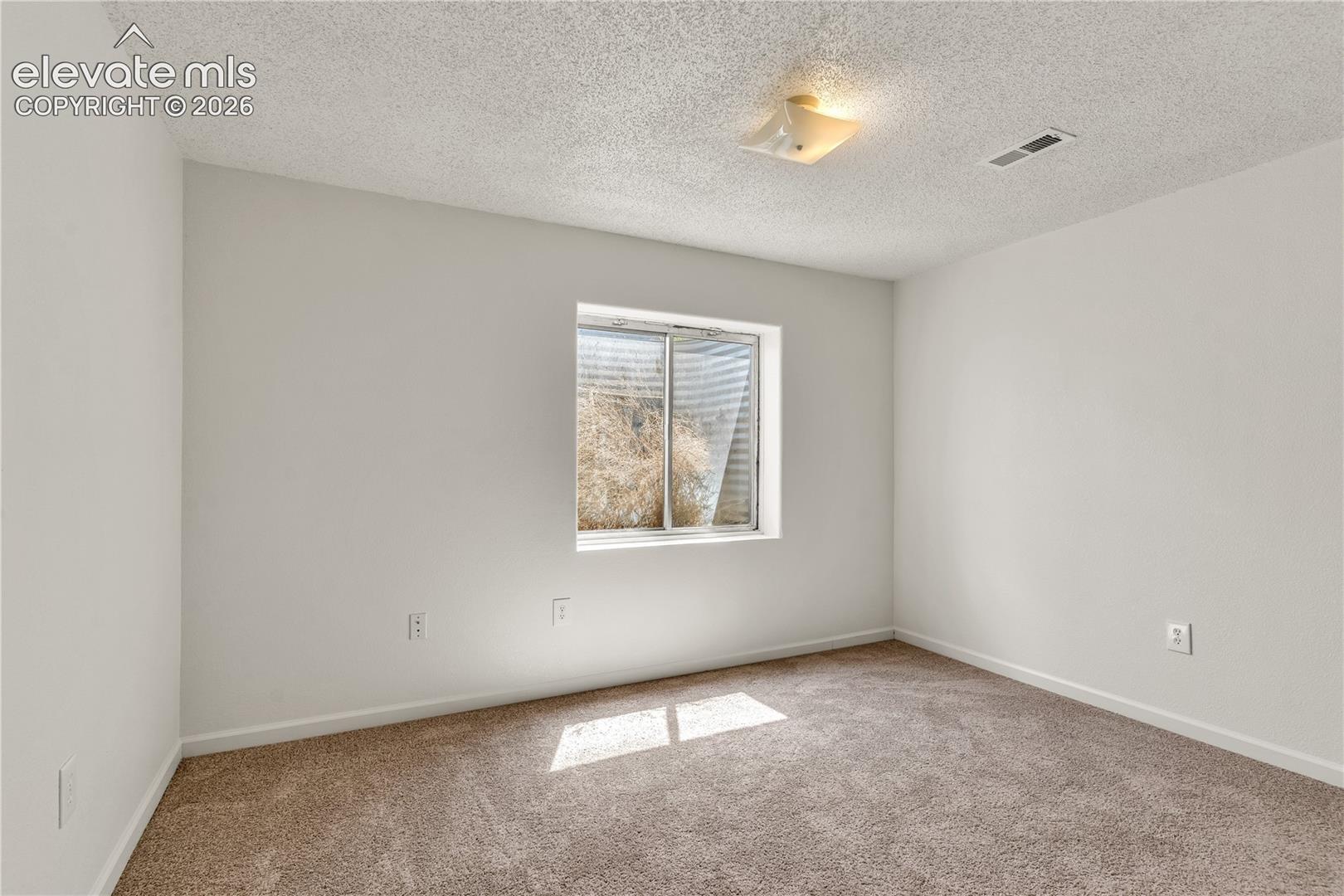 Neutral wall finishes with a single window, overhead lighting, and carpeted flooring