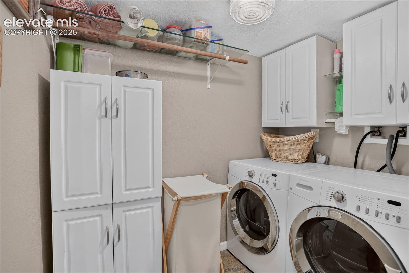 Dedicated laundry space with built-in white cabinetry, glass shelving, and neutral wall tones