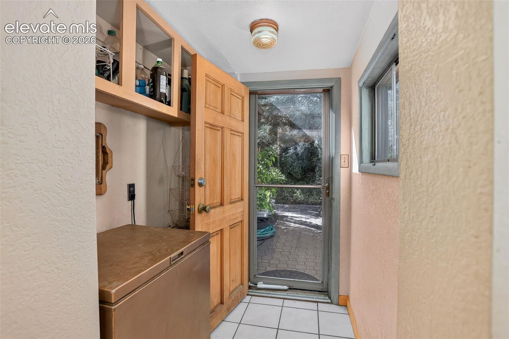 Wood-panel door, white tile flooring, built-in upper cabinetry, and a window providing natural light