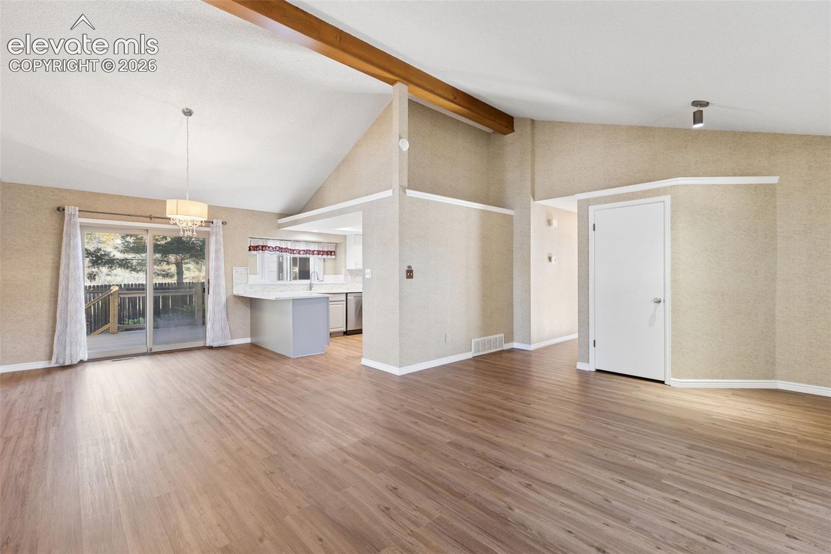 Vaulted ceilings with exposed wooden structural beams, wood-finish flooring, sliding glass doors, and recessed lighting