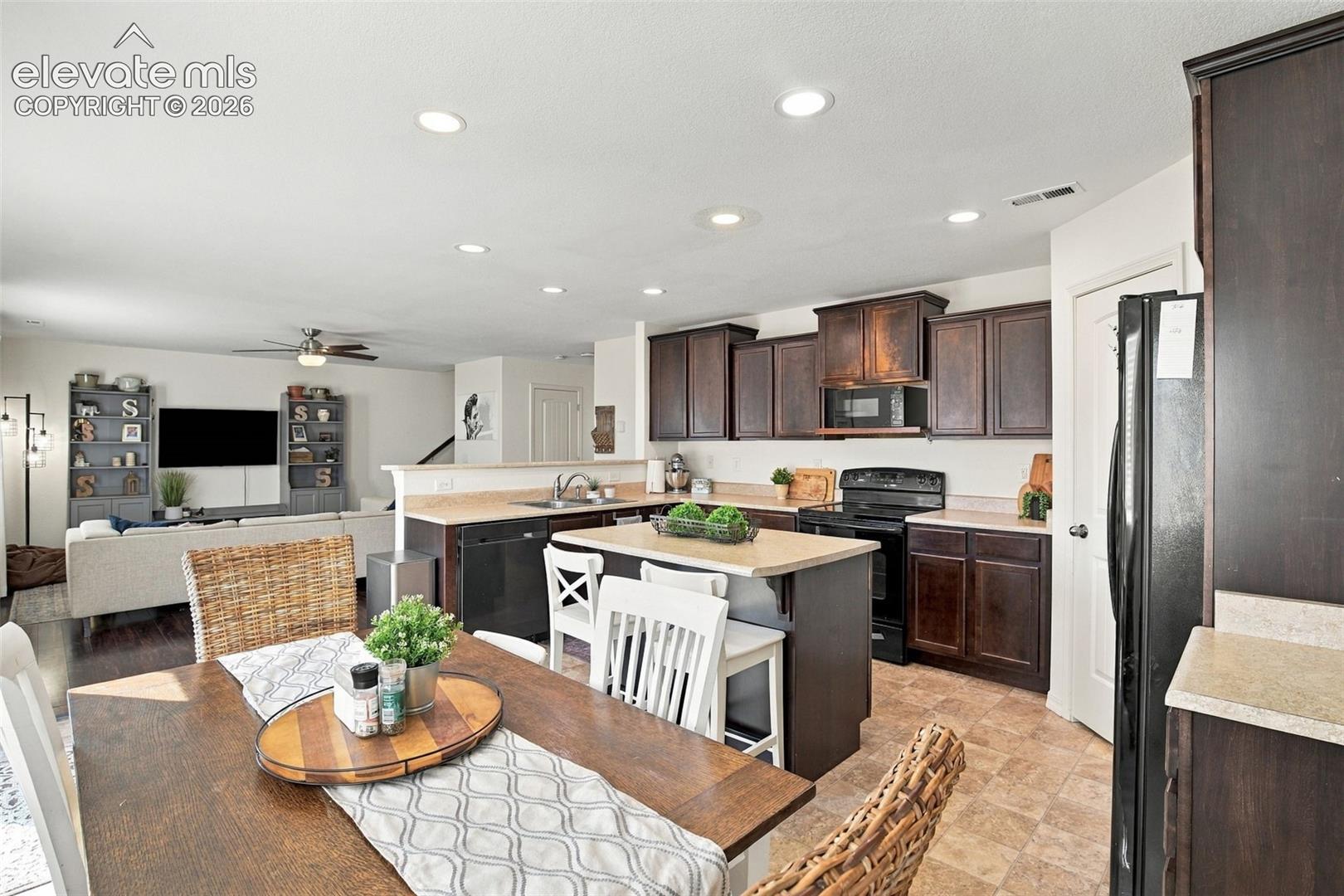 Open-concept kitchen and dining area featuring recessed lighting, a kitchen island with countertop seating, dark wood-finish cabinetry, and black appliances