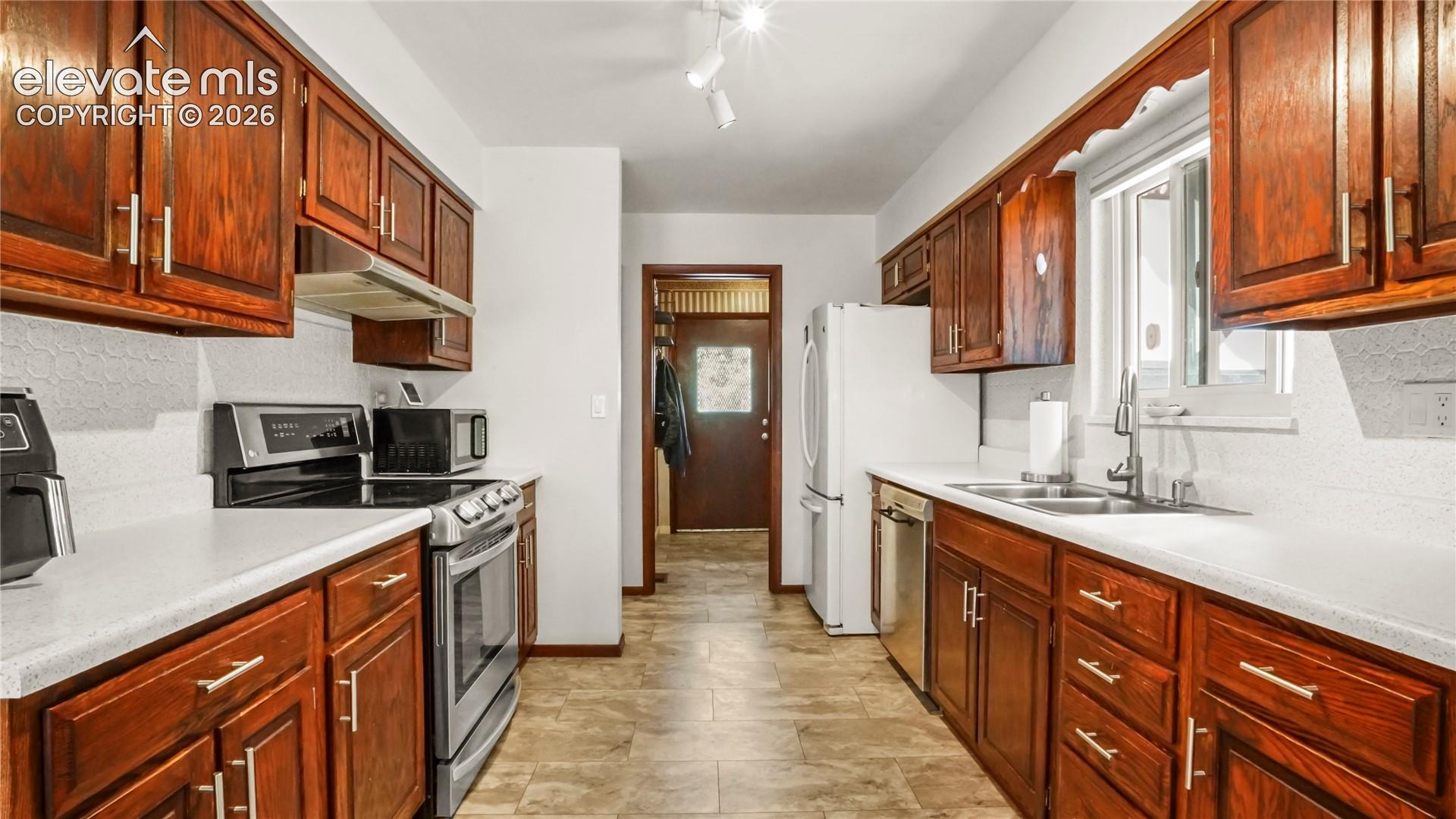 Galley kitchen featuring wood cabinetry, white countertops, and appliances