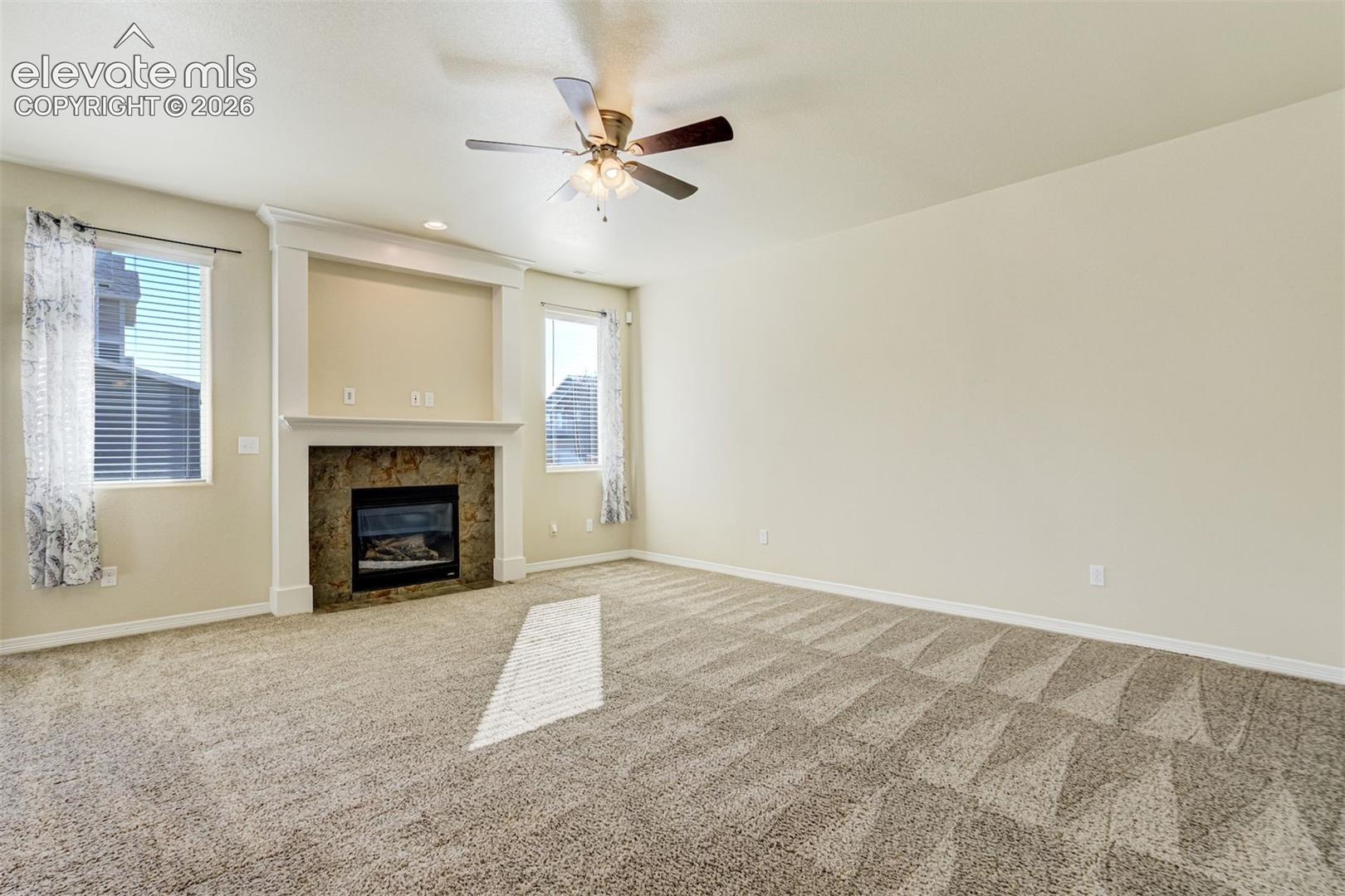 Spacious room featuring, a ceiling fan with integrated lighting, and a stone-surround fireplace with a built-in mantel and media niche