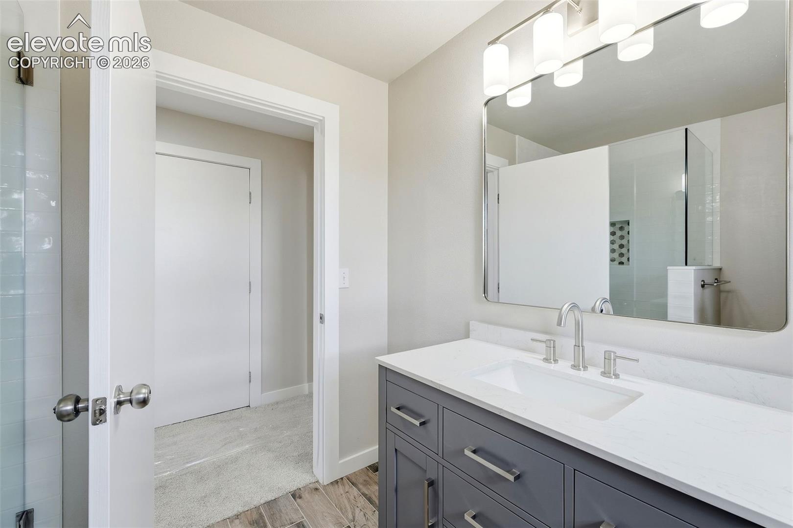 Vanity with a white countertop and undermount sink, wood-finish flooring, and a large wall mirror with integrated lighting