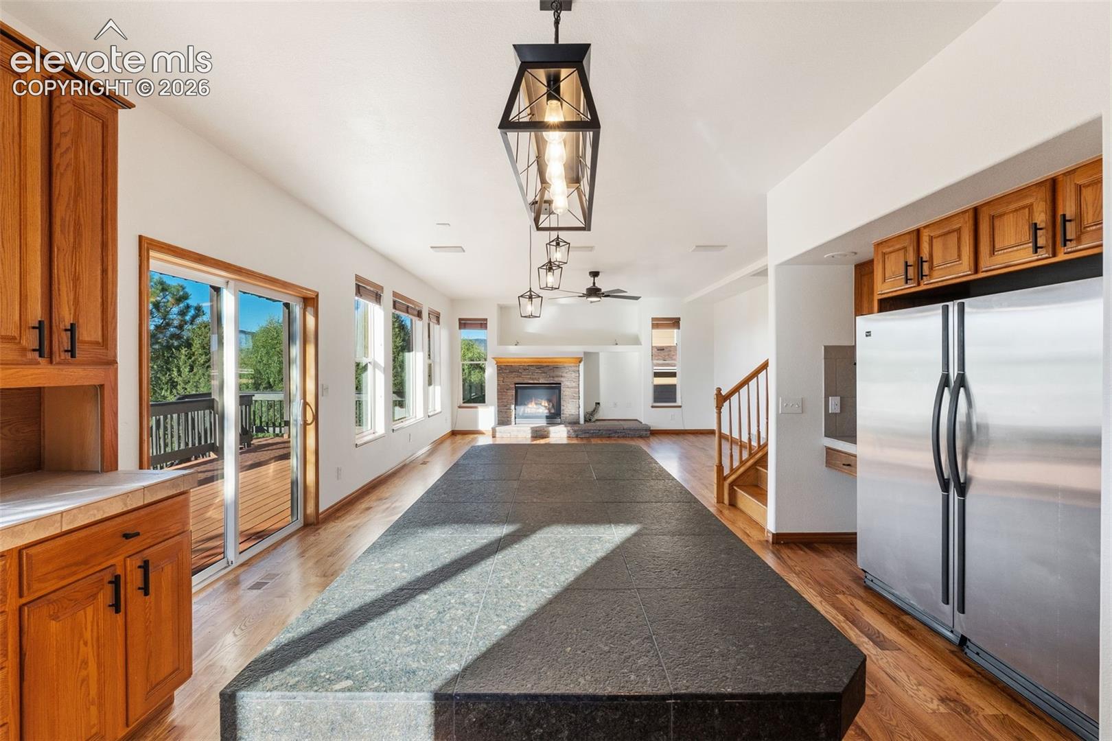 Kitchen featuring wood cabinetry, expansive stone-topped island, stainless steel refrigerator, wood-finish flooring, and a stone-surround fireplace