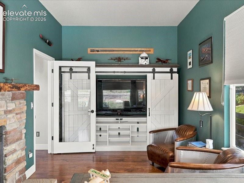 Built-in entertainment center with sliding barn doors, wood-finish flooring, and a stone-clad fireplace