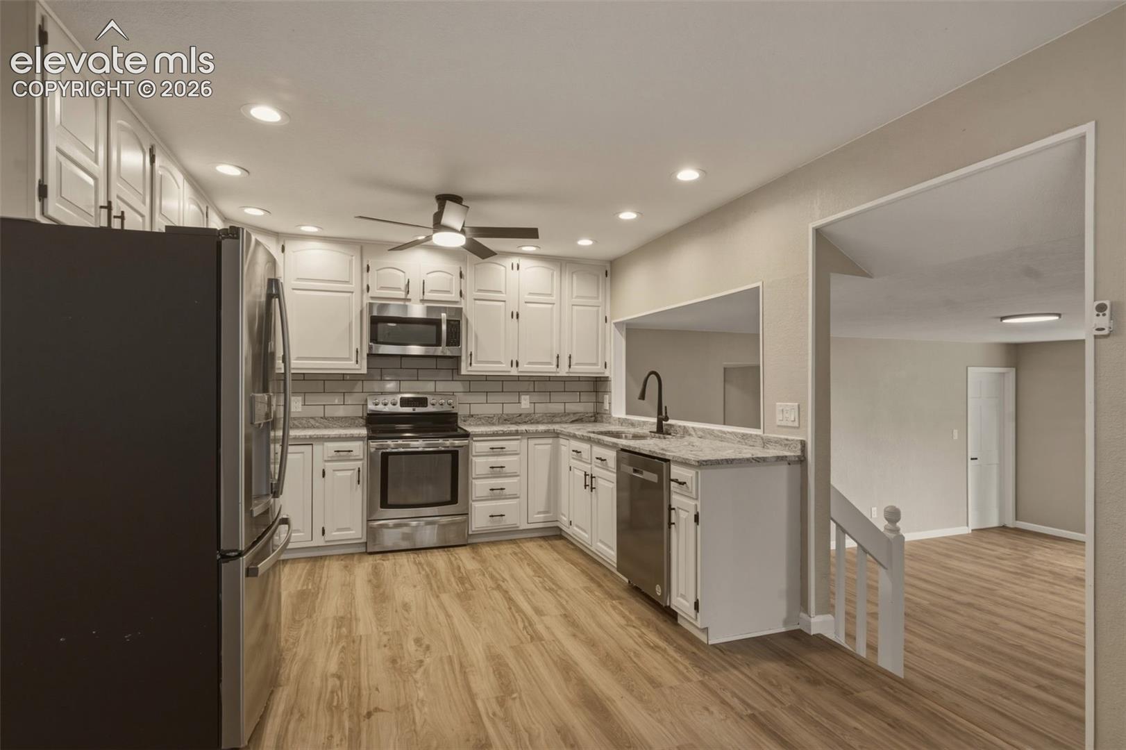 Contemporary kitchen featuring wood-finish flooring, white cabinetry, integrated stainless-steel appliances, a subway tile backsplash, and recessed lighting