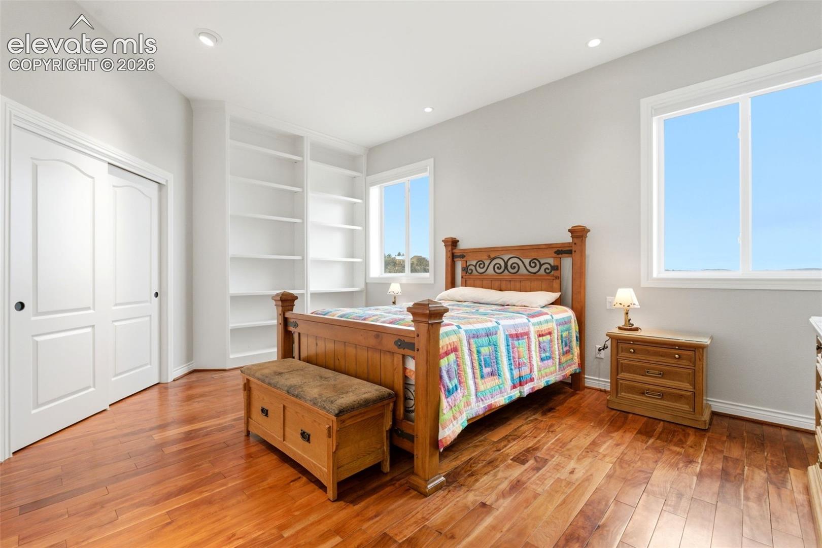 Wood-finish flooring, recessed lighting, built-in shelving, and white framed windows