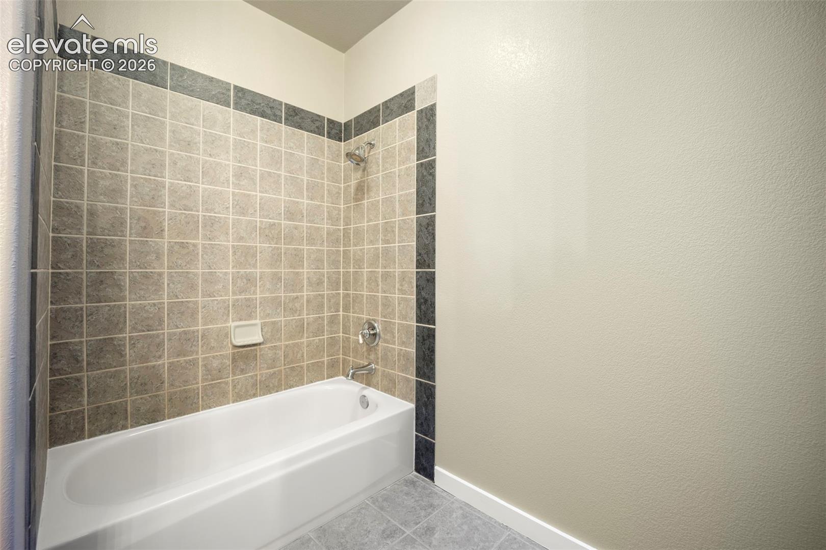 Bathtub with a tiled surround featuring light-toned square tiles and a dark accent border