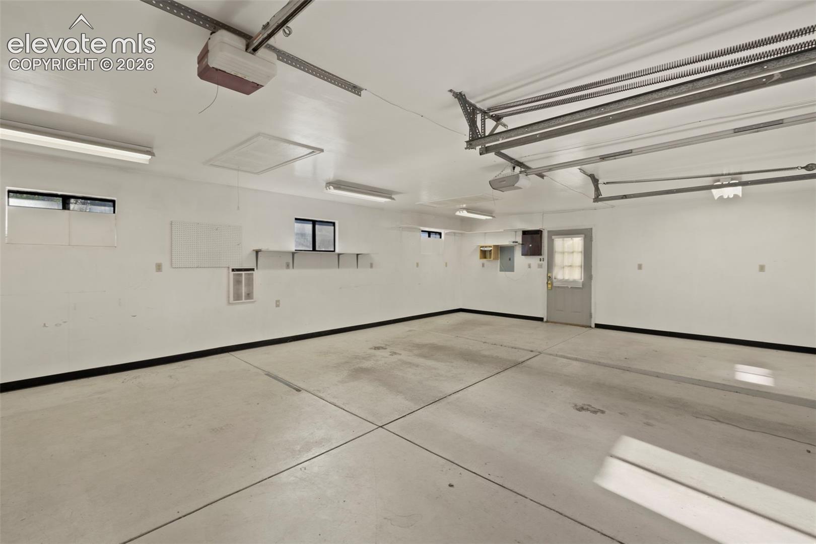 Spacious garage featuring a concrete floor, multiple fluorescent light fixtures, two windows, and an exterior access door with a frosted glass panel