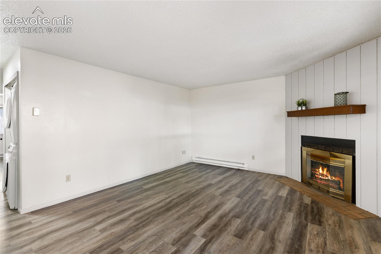 Living area featuring wood-finish flooring, a fireplace with a brass-trimmed insert, and a white paneled accent wall with a wooden mantel