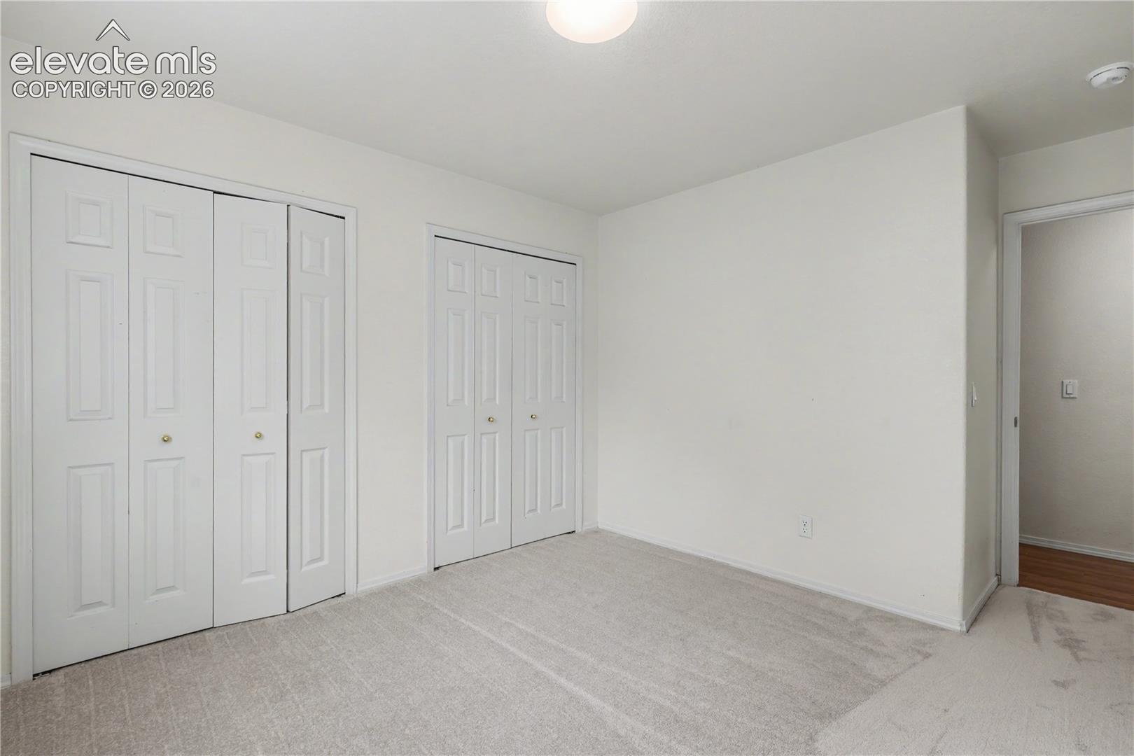 Carpeted room featuring two sets of bi-fold closet doors with brass-toned hardware, white walls, and a ceiling-mounted light fixture