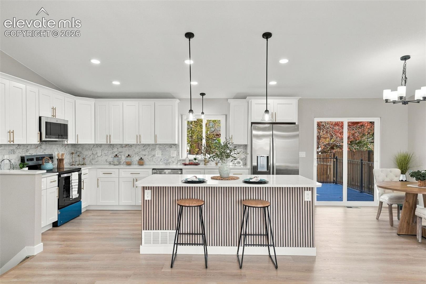 Kitchen featuring white shaker cabinetry, stone-patterned backsplash, center island with vertical slat detailing, stainless steel appliances, and wood-finish flooring