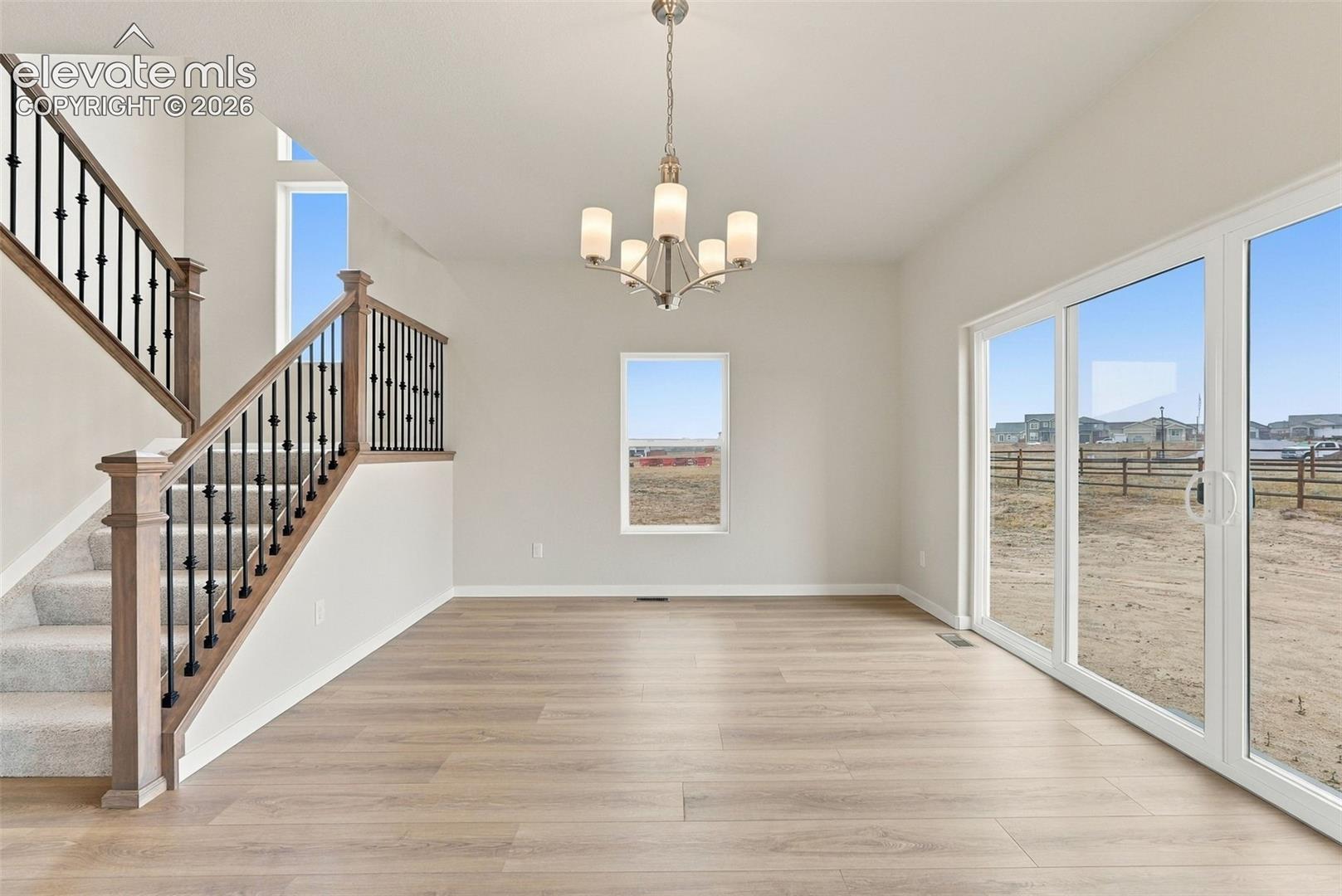 Wood-finish flooring, staircase with wood handrail and iron balusters, sliding glass patio doors, and a multi-arm chandelier