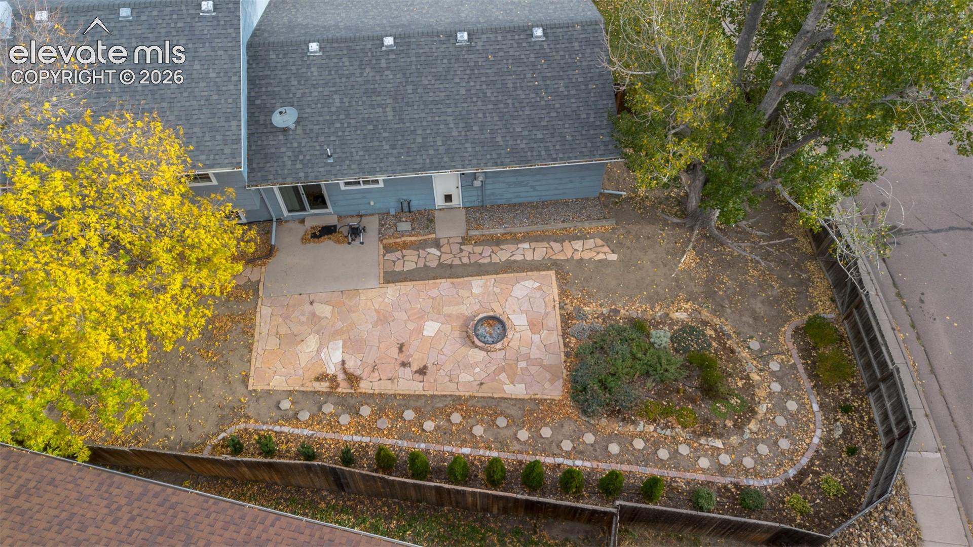 Backyard featuring a stone-paver patio, built-in circular fire pit, stone-accented pathways, mature trees, and wooden perimeter fencing