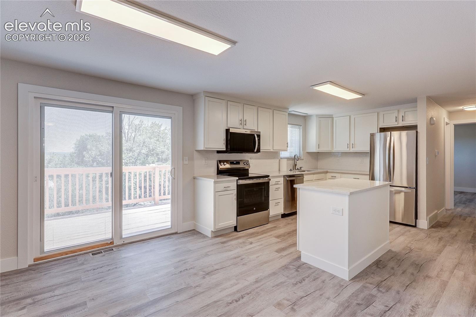 Kitchen featuring white shaker-style cabinetry, wood-finish flooring, a central island, stainless steel appliances, and a sliding glass door