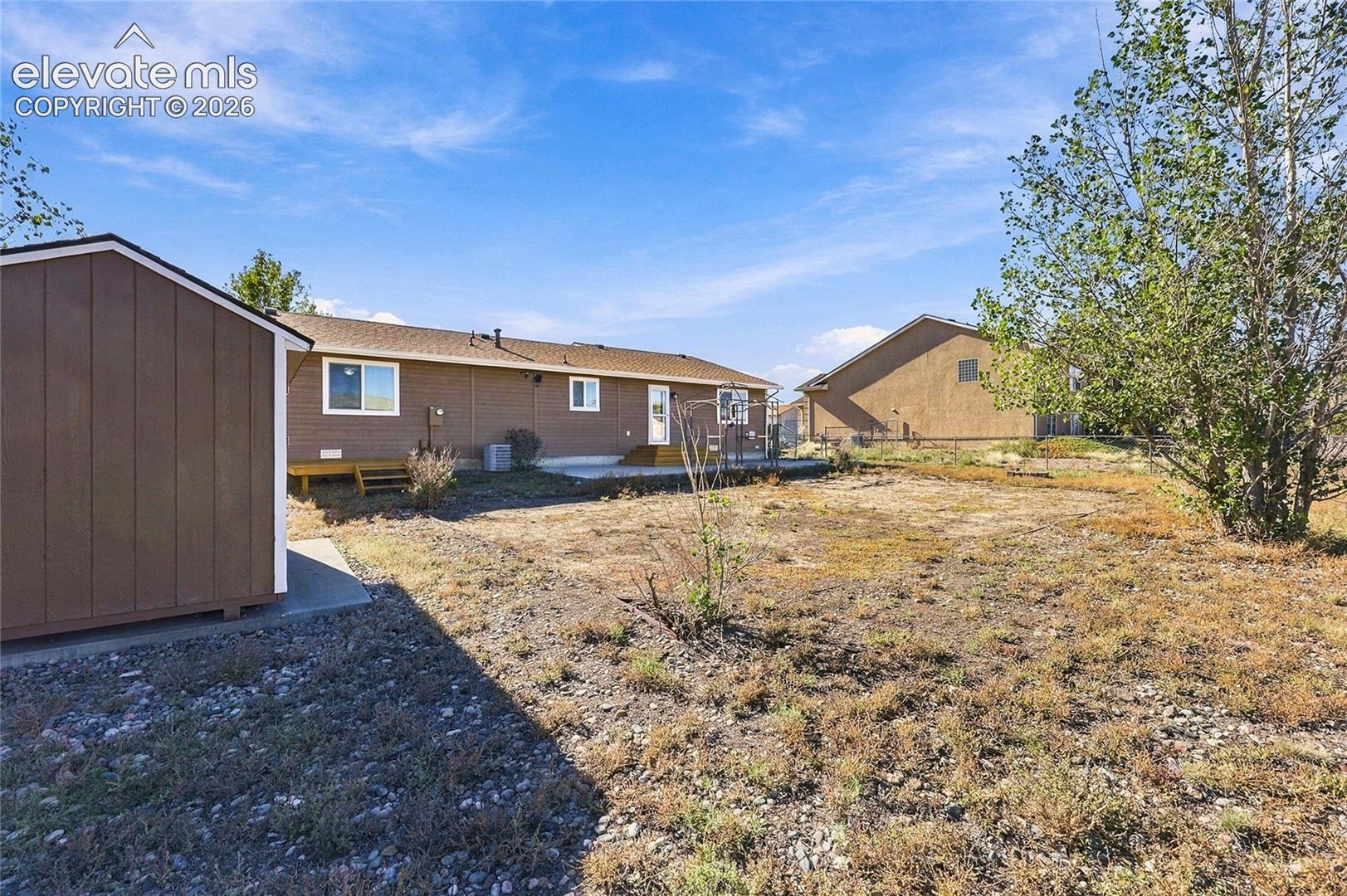 Rear exterior featuring a detached wood-sided storage shed, concrete patio, and fenced-in grounds with mature trees