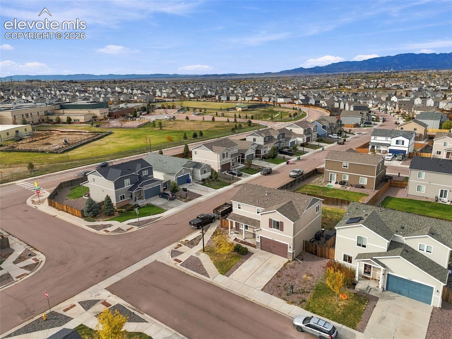 Aerial perspective of a multi-level residence featuring a concrete driveway, two-car garage, asphalt shingle roof, and mountain backdrop