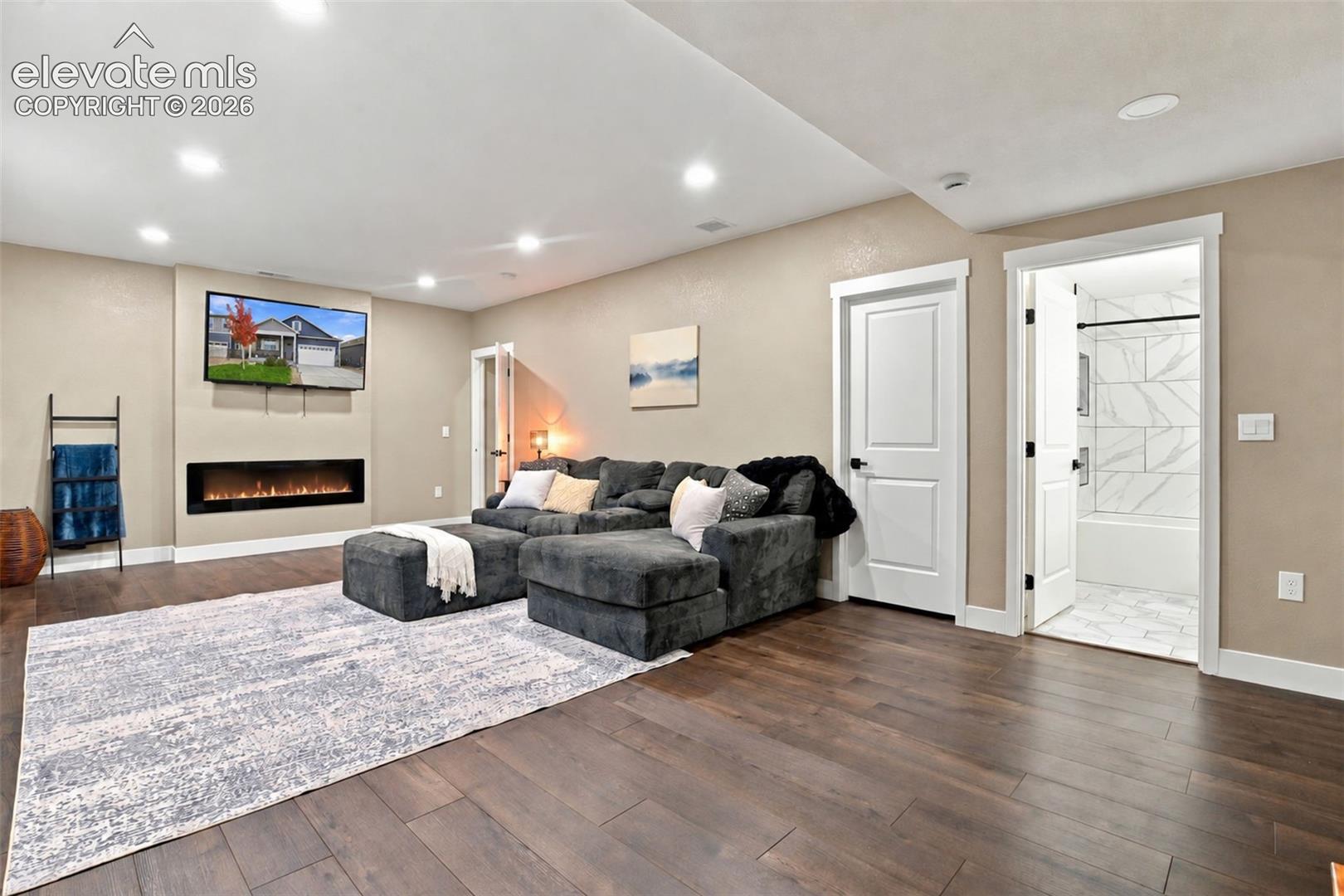 Recessed lighting, wood-finish flooring, built-in horizontal electric fireplace, and paneled doors