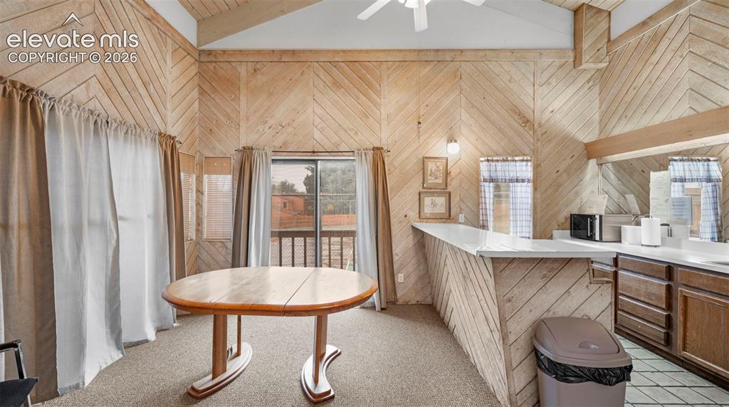 Vaulted wood-paneled ceilings with exposed beams, wood-finish wall paneling, built-in bar, and glass sliding door access to an exterior deck