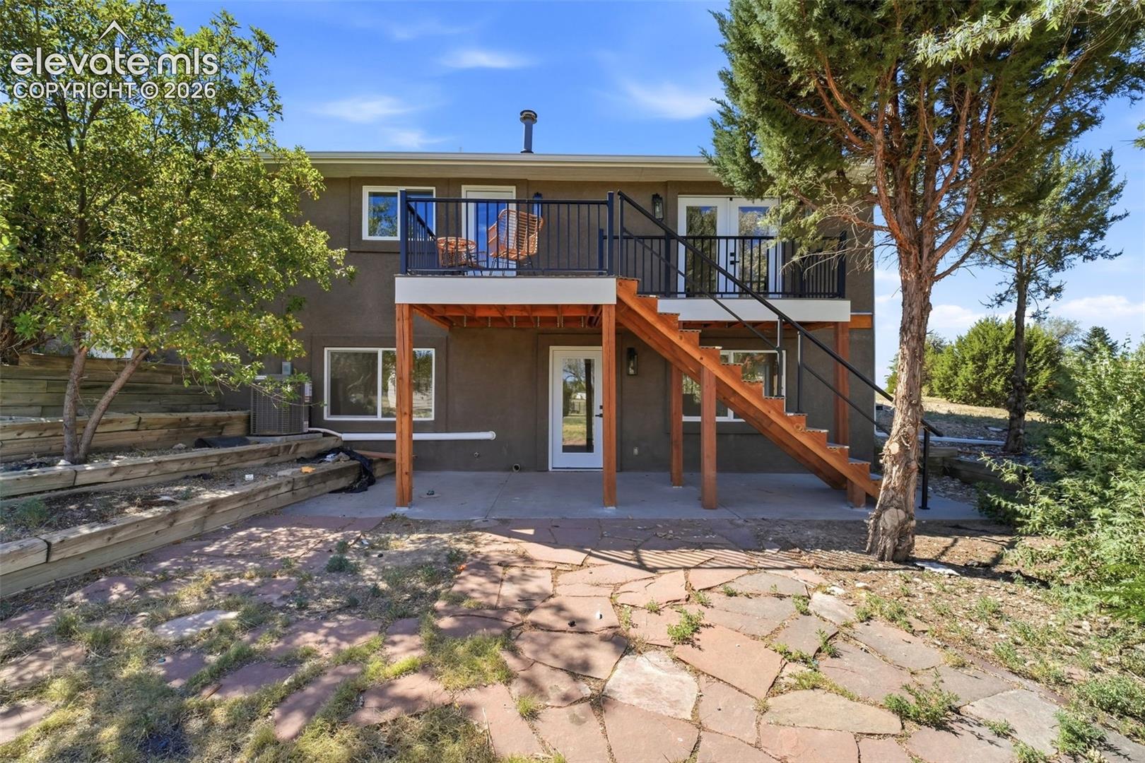 Multi-level deck and patio area featuring a wooden staircase, black metal railings, and a flagstone patio