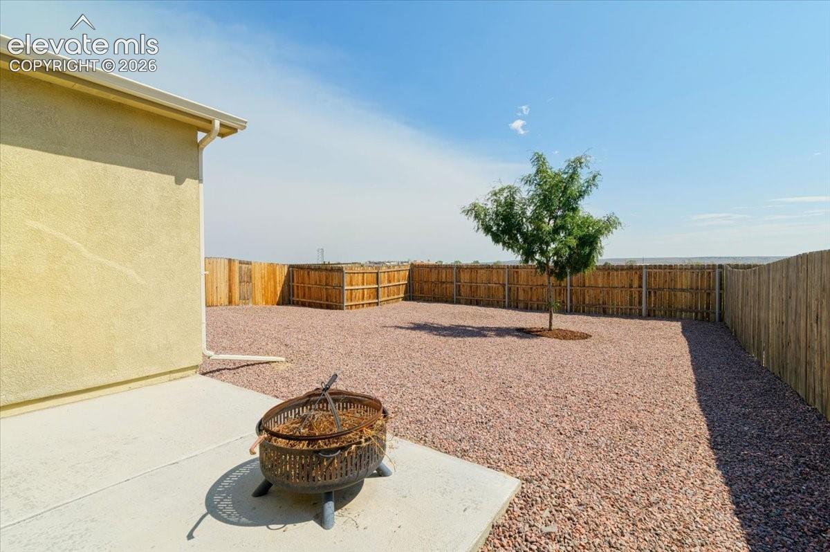 Stucco exterior, concrete patio, gravel hardscaping, privacy fencing, and a mature tree