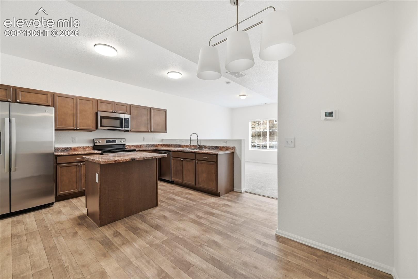 Kitchen featuring wood-finish flooring, shaker-style cabinetry, an island, stone-patterned countertops, and stainless steel appliances