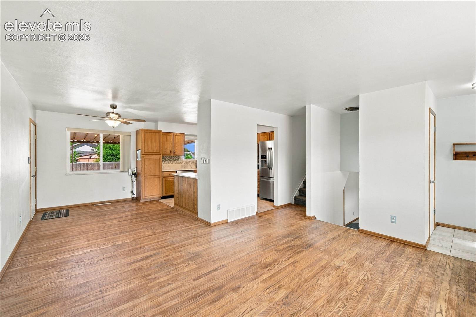 Open-concept living area with wood-finish flooring, white walls, and a ceiling fan