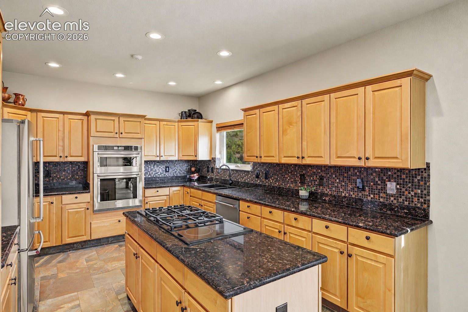 Spacious kitchen featuring warm wood cabinetry, granite countertops, tile backsplash, center island with gas cooktop, double wall ovens, and recessed lighting.