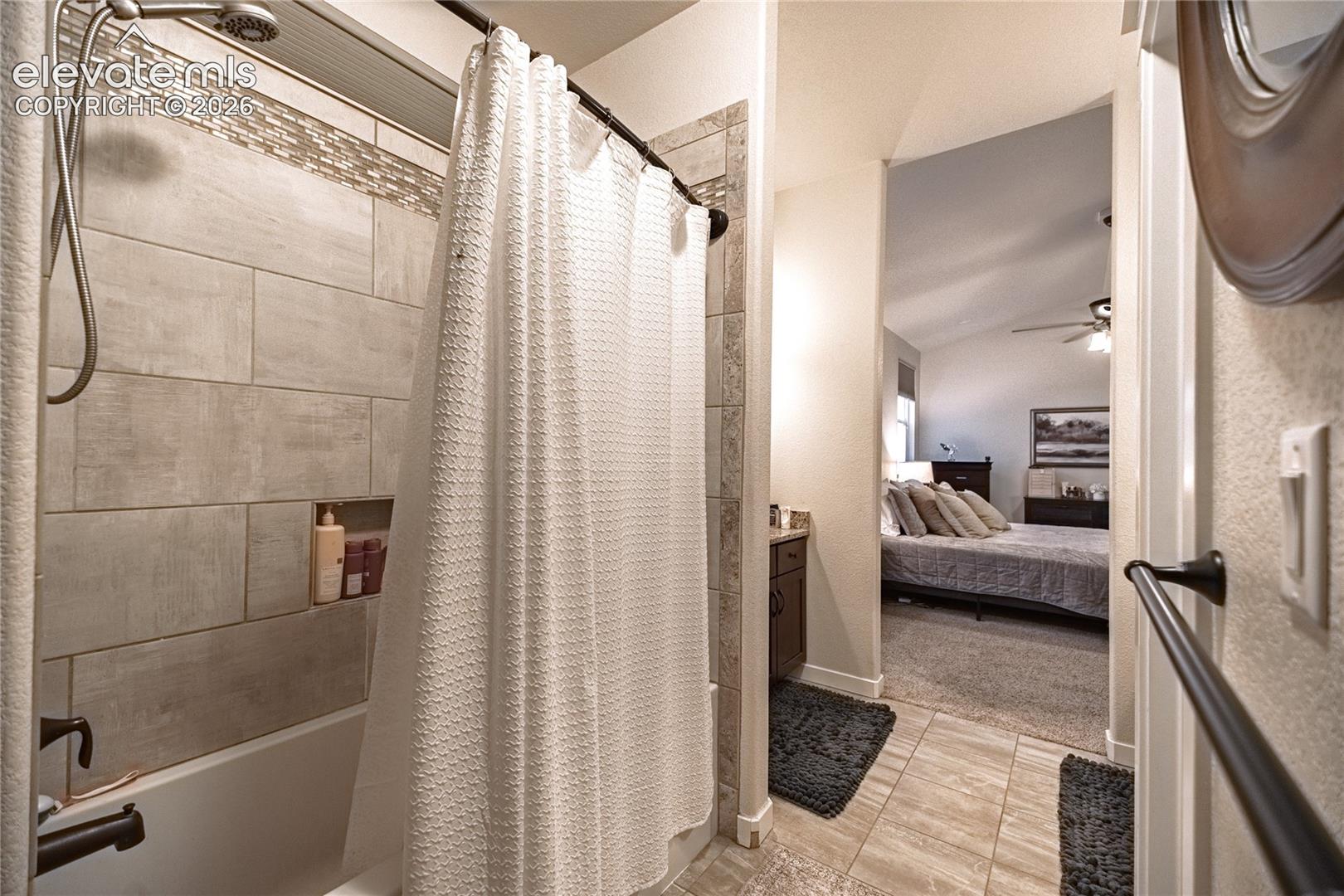 Bathroom featuring a tile-surround shower with built-in recessed shelving, a handheld showerhead, dark-finish hardware, and floor tile